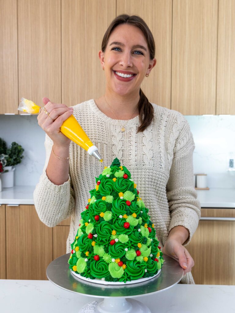 image of chelsey white of chelsweets piping buttercream frosting onto a Christmas tree cake