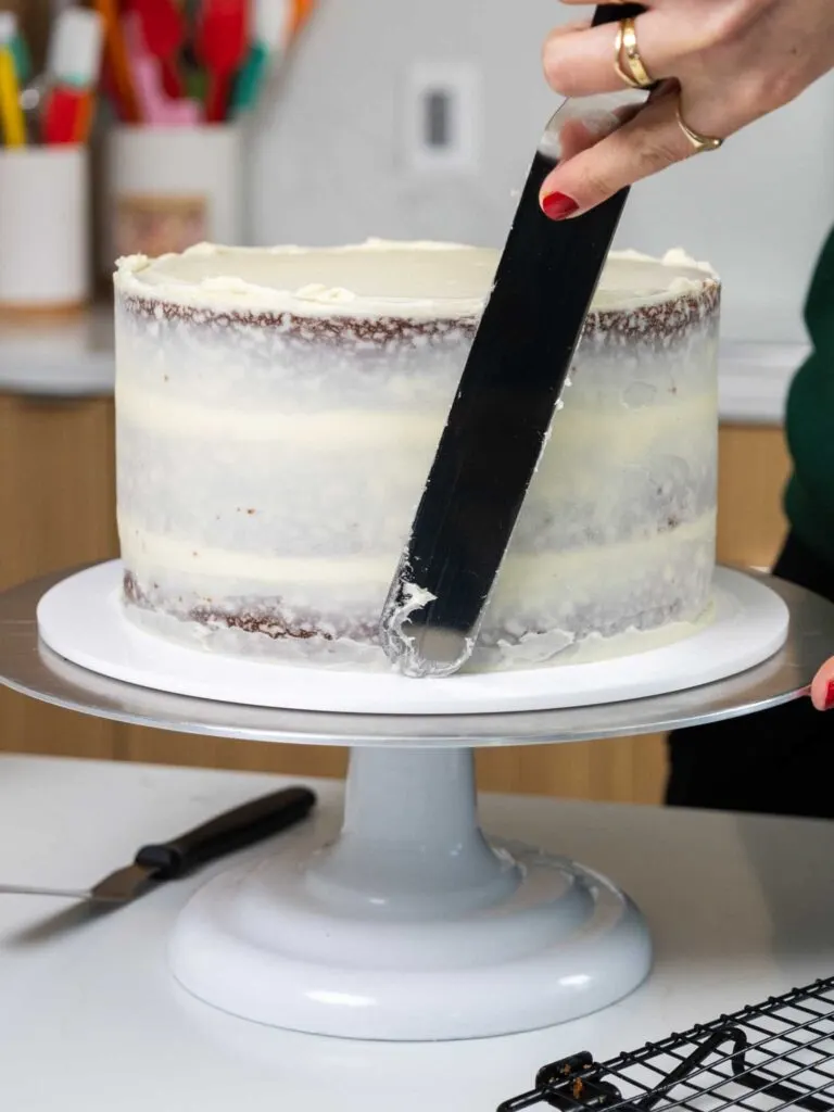 image of of a gingerbread layer cake being crumb coated with cream cheese frosting