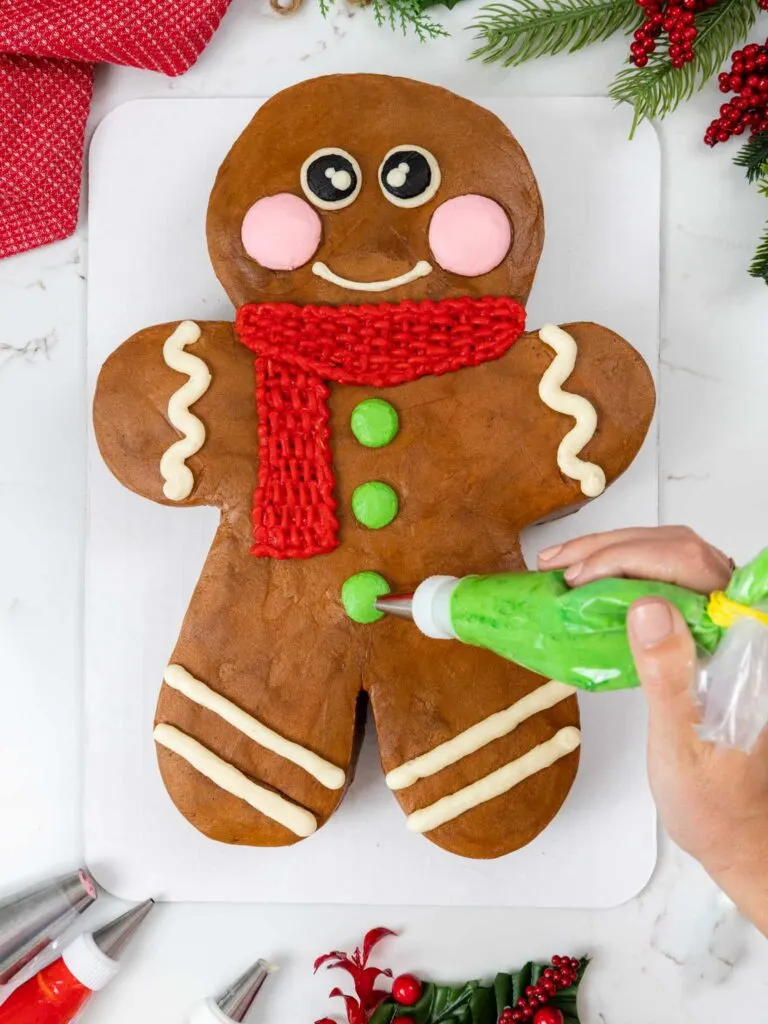 image of buttercream buttons being piped onto a gingerbread man cake