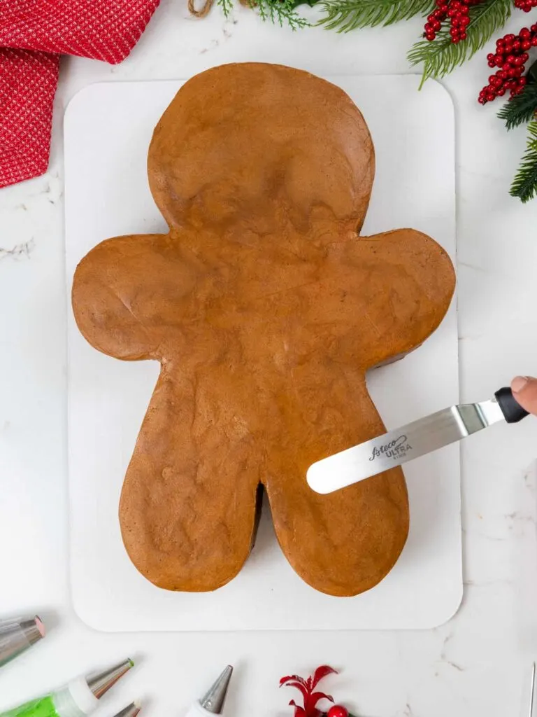image of gingerbread buttercream being smoothed onto a gingerbread man shaped sheet cake