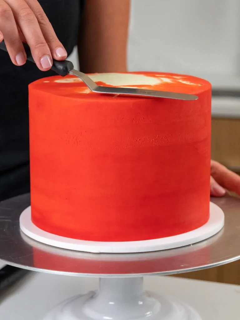 image of red buttercream frosting being smoothed on a cake