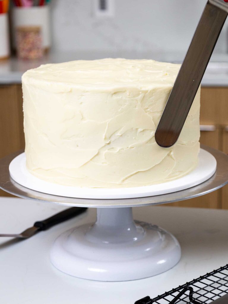 image of cream cheese frosting being spread on a gingerbread cake with a large offset spatula