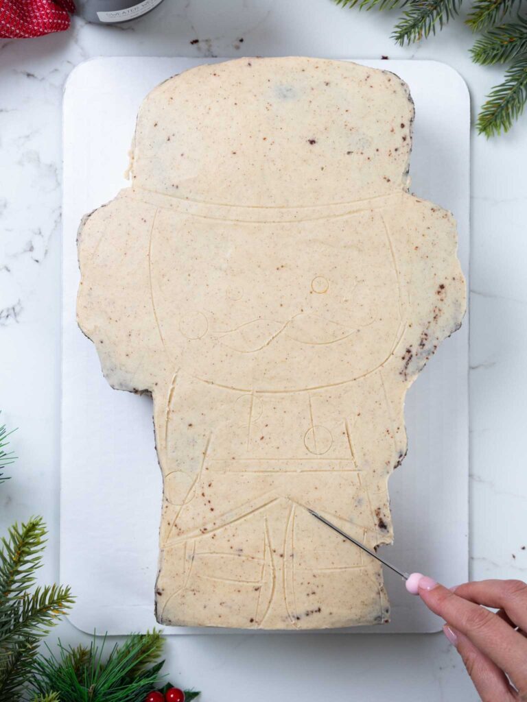 image of the outline of a nutcracker cake being traced out on a chocolate sheet cake that's been crumb coated in peanut butter buttercream