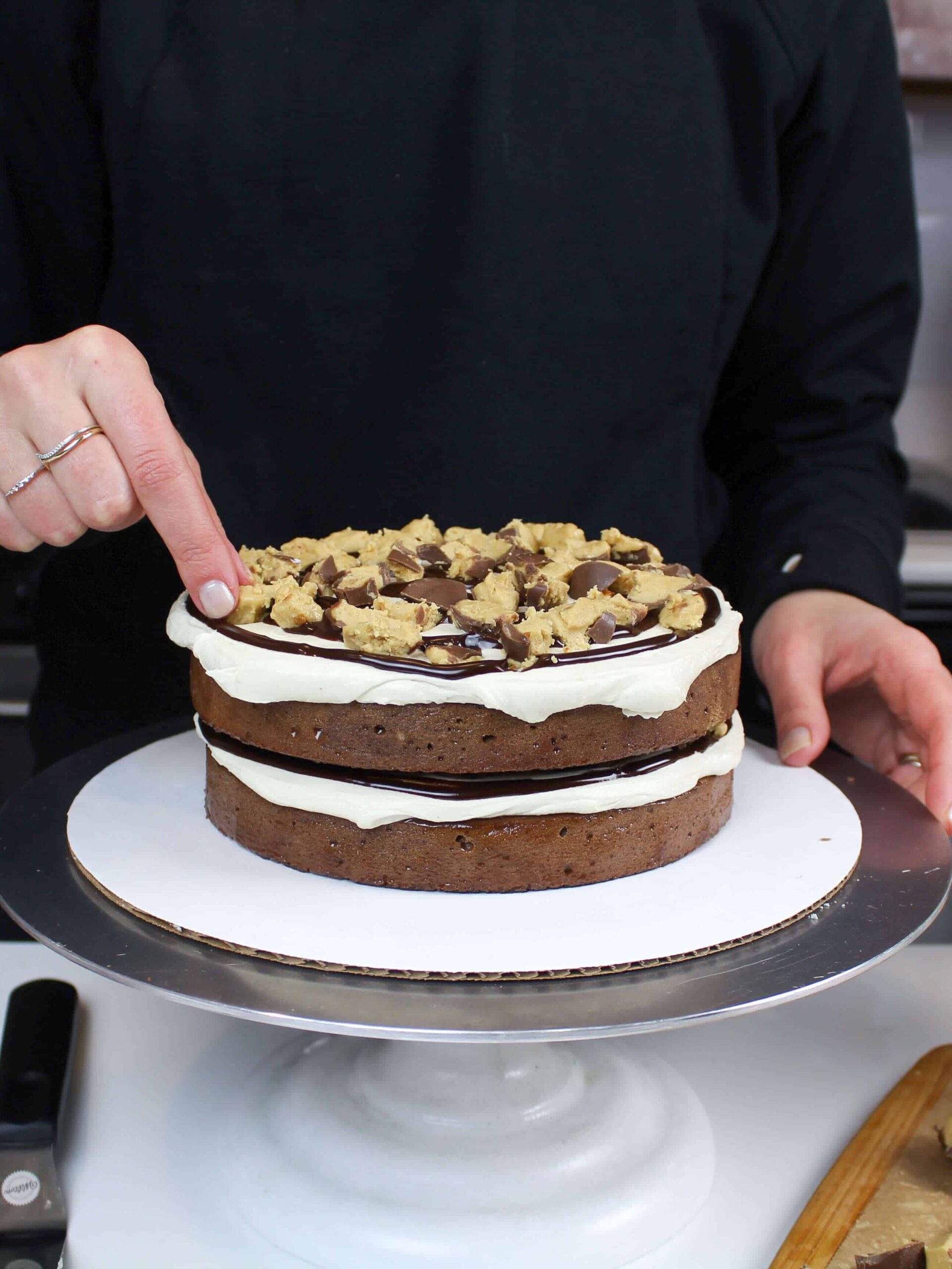 image of a buckeye cake being assembled with chocolate cake layers, peanut butter frosting and filled with chopped up pieces of buckeye.
