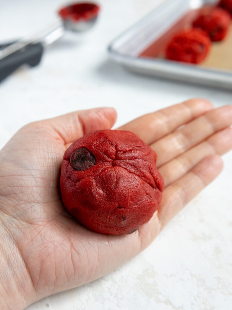 image of red velvet cookie dough that's been stuffed with Nutella and rolled into a ball and is ready to be baked