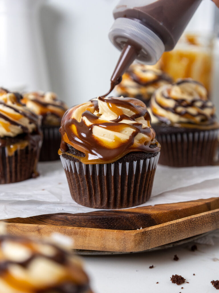 image of chocolate ganache being drizzled over a chocolate caramel cupcake