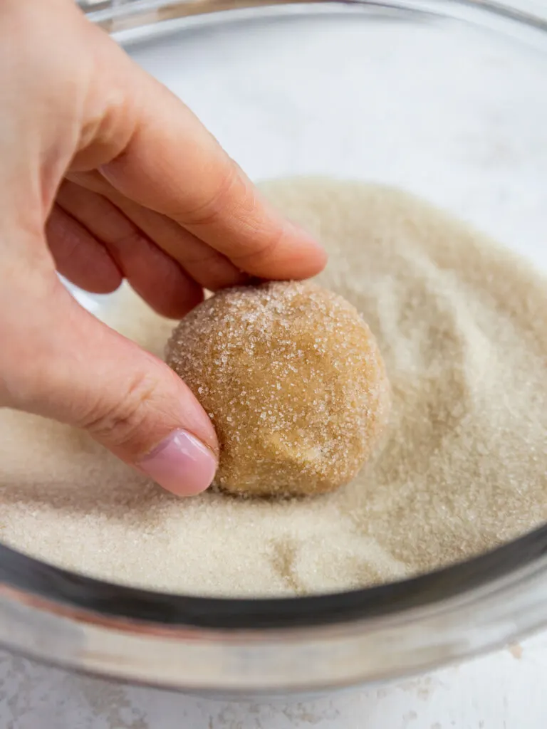 image of a peanut butter cookie being rolled in granulated sugar