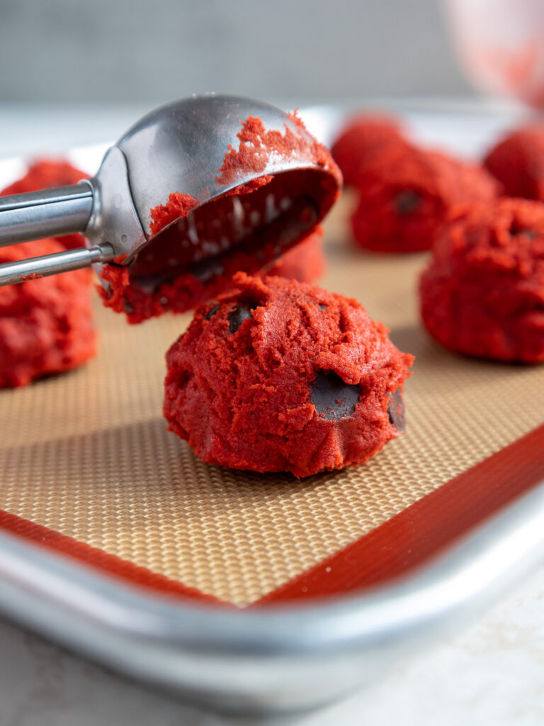 image of red velvet cookie dough being scooped with a cookie scoop