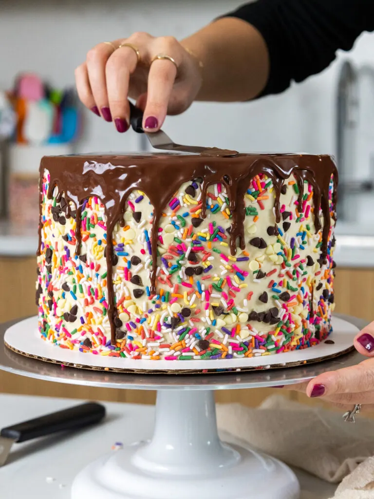 image of chocolate ganache drips being added to a cake with an offset spatula