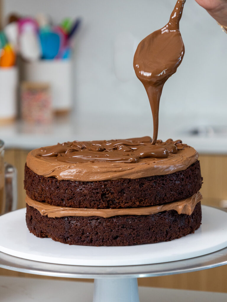 image of Nutella being drizzle over Nutella buttercream and chocolate cake layers to make a Nutella cake