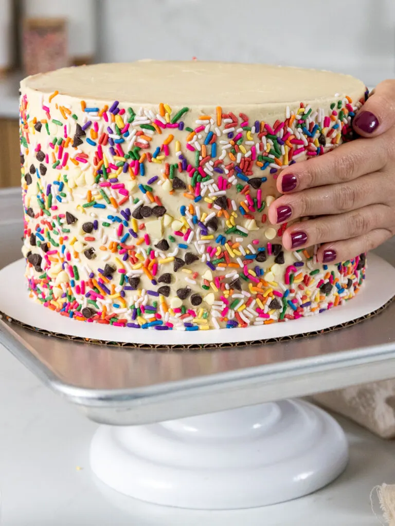 image of sprinkles and mini chocolate chips being added to the side of a cookie dough cake