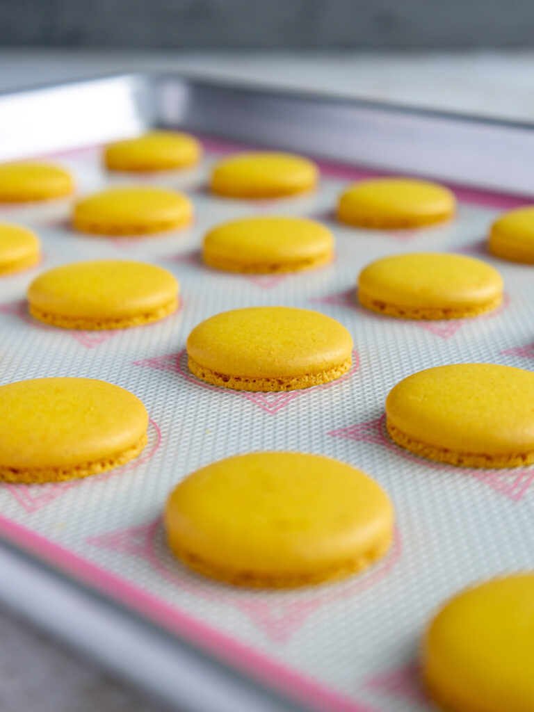 yellow macaron shells that have been baked and are cooling on a silpat mat