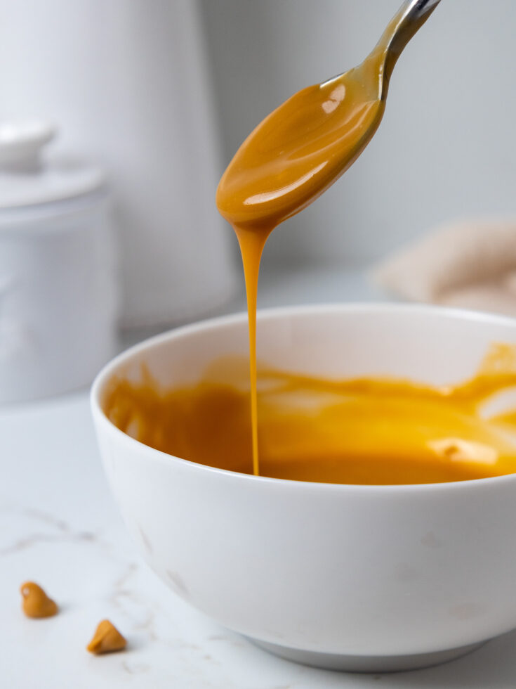 image of butterscotch ganache being stirred with a spoon and drizzled to test its consistency
