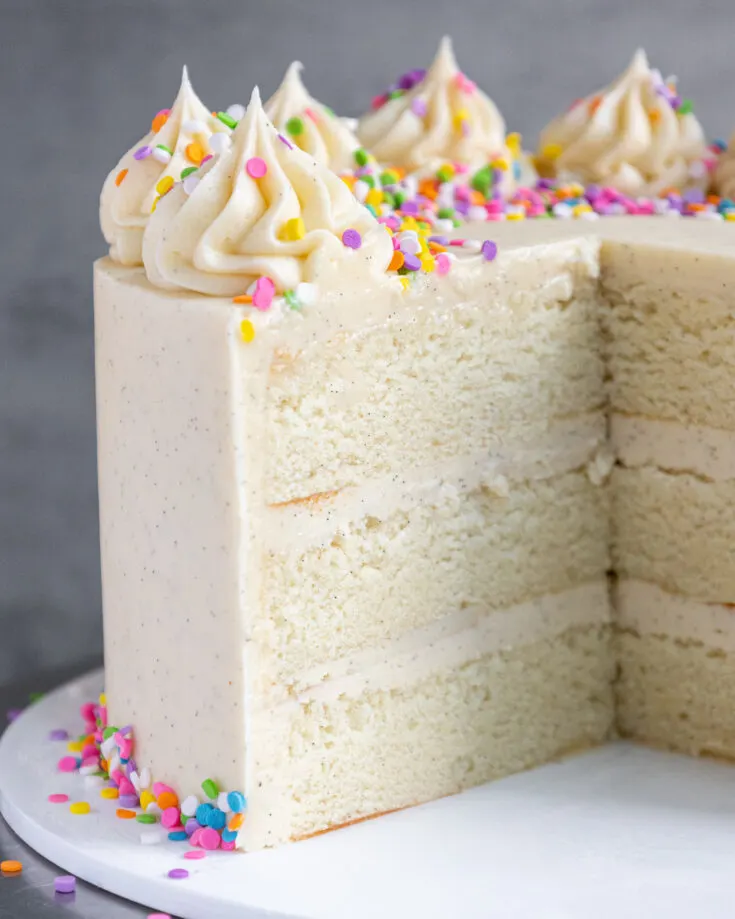 image of a vanilla bean cake that's been cut into to show its tender cake layers and beautiful vanilla bean speckles