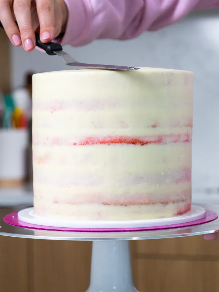 a pink velvet cake that has been crumb coated with cream cheese buttercream frosting
