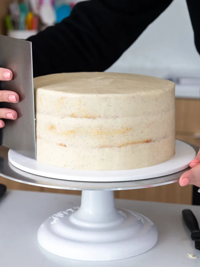 image of a vanilla bean cake being crumb coated with buttercream frosting