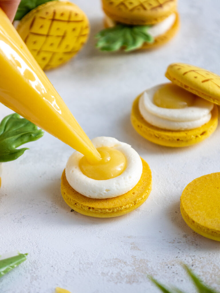 yellow macaron shell being filled with a ring of cream cheese buttercream and pineapple curd
