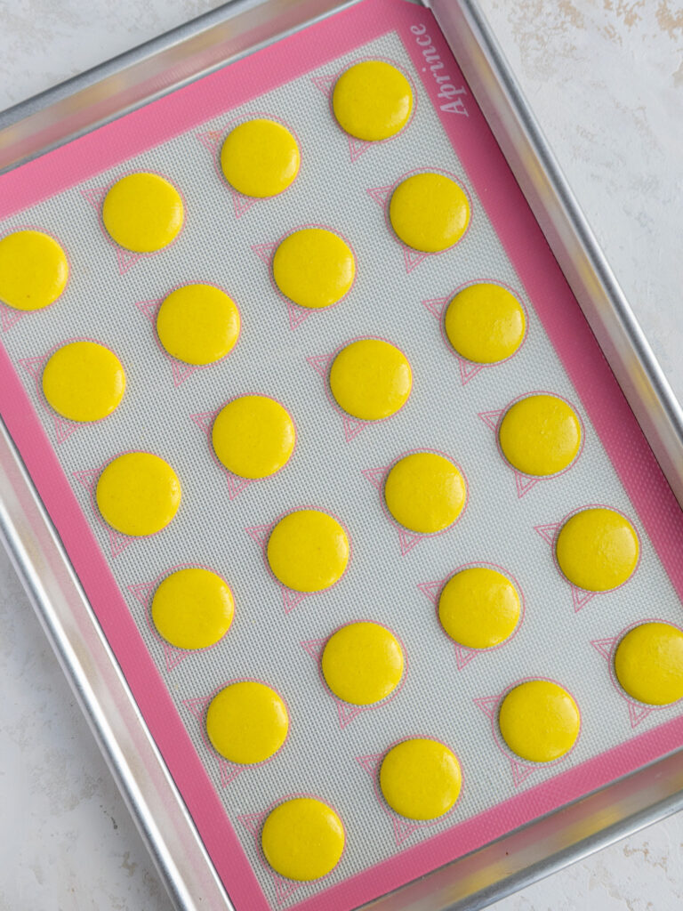 overhead shot of yellow macaron shells that have been piped on a silpat mat and are resting before being baked