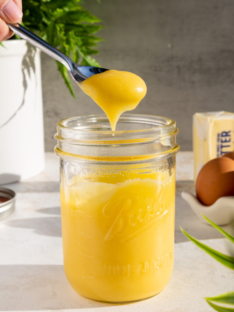 pineapple curd that's being spooned out of a mason jar to show its thick texture