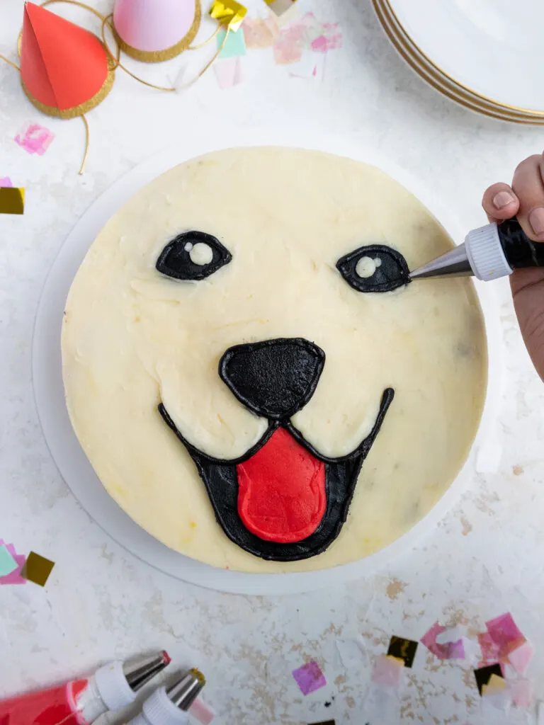 image of black and red buttercream being piped onto a cake to look like the face of a golden retriever