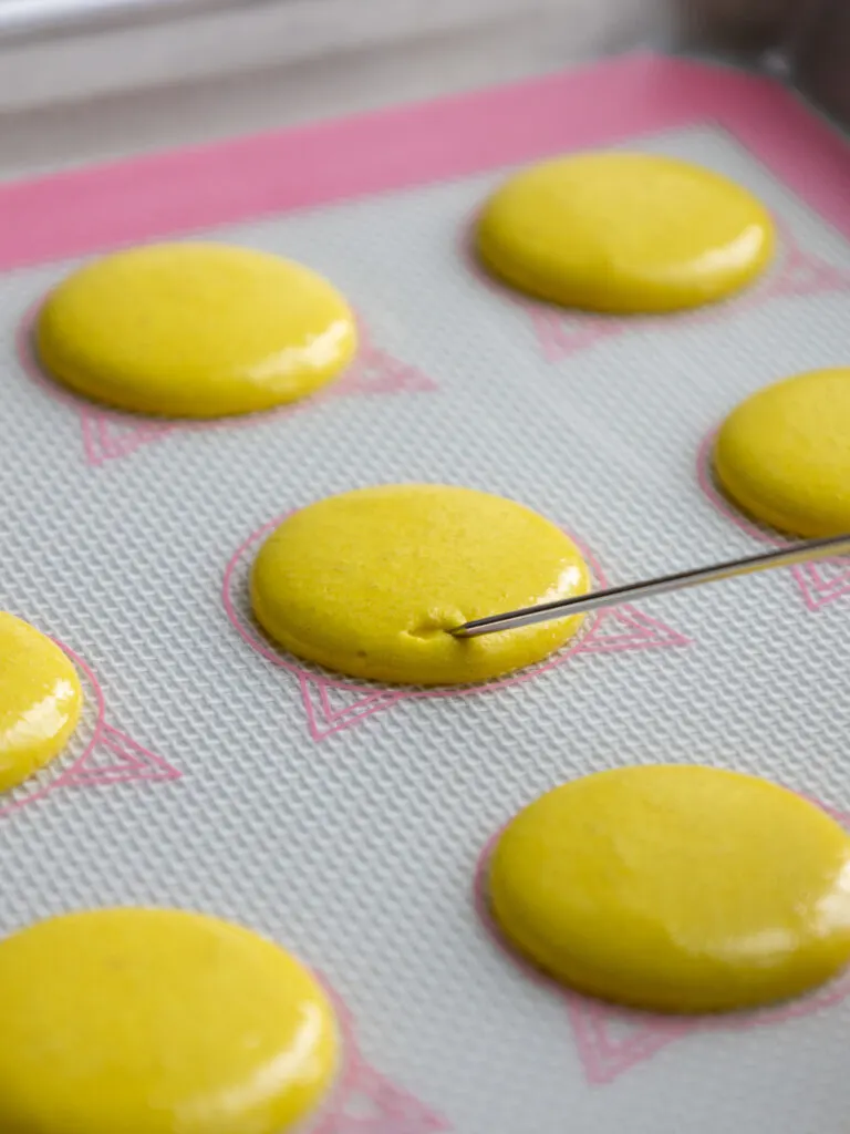 using a scribe to pop little air bubbles in yellow french macaron shells