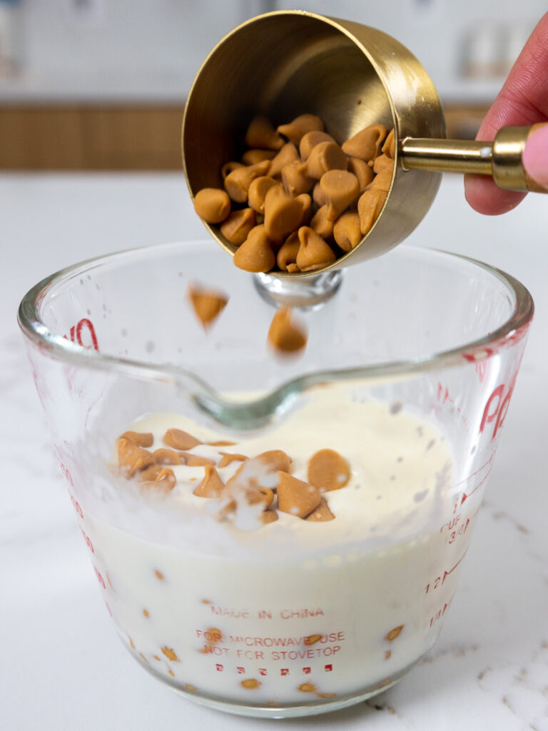 image of butterscotch chips being poured into a heat proof container with heavy cream