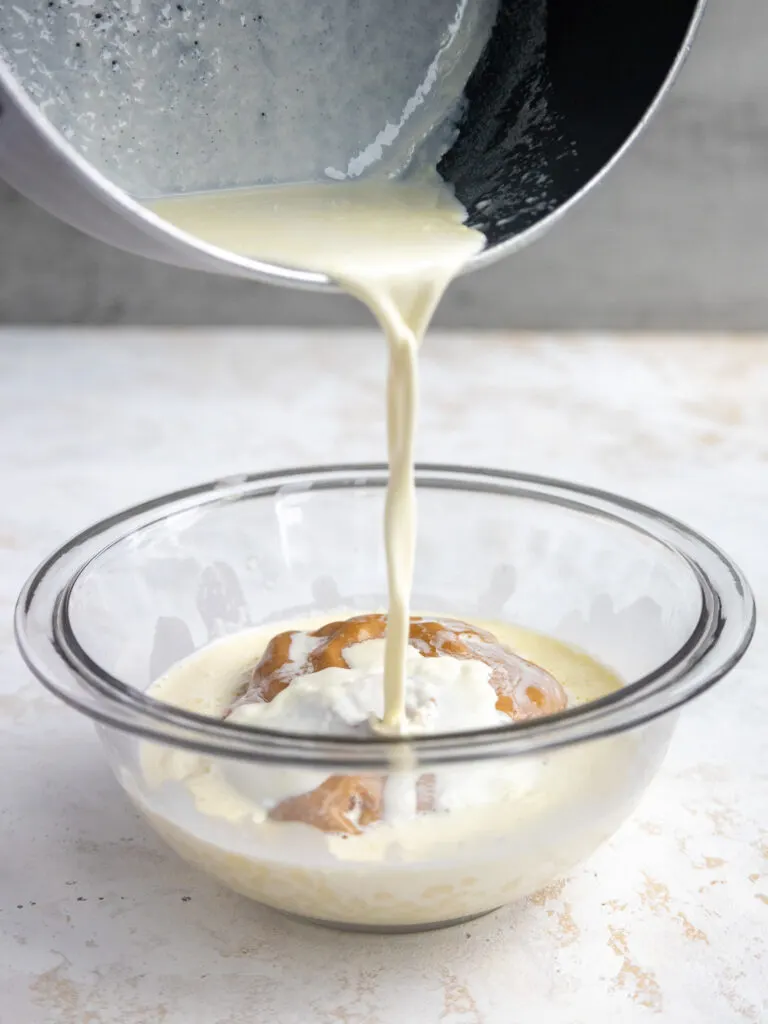 hot cream being poured over white chocolate and peanut butter in a glass bowl