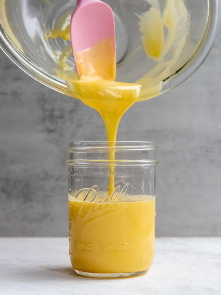 cooked pineapple curd being poured into a mason jar to cool and be stored in the fridge