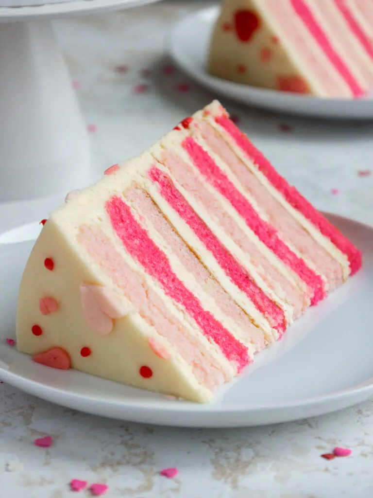 slice of pink velvet cake on a plate that's been frosted with cream cheese buttercream frosting