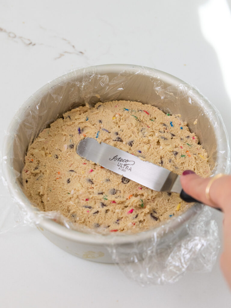 image of edible cookie dough being smoothed out in a lined cake pan to make edible cookie dough discs