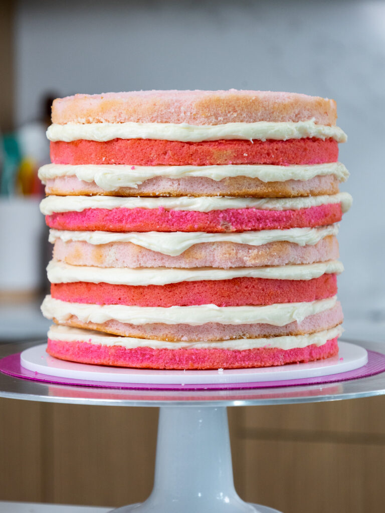 image of 8, thin, pink velvet cake layers that have been stacked with cream cheese buttercream frosting