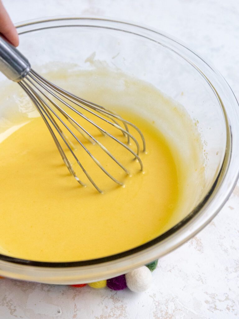 cooked pineapple curd being stirred in a glass bowl after having had butter mixed into it