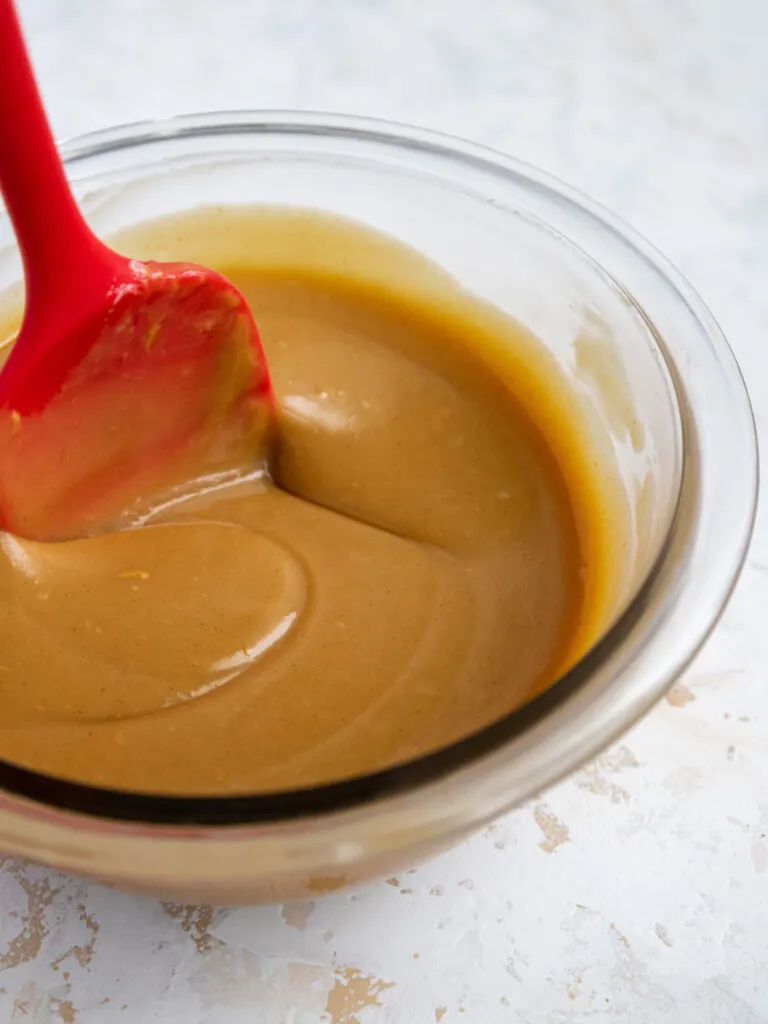 image of peanut butter ganache being stirred together in glass bowl with a red spatula