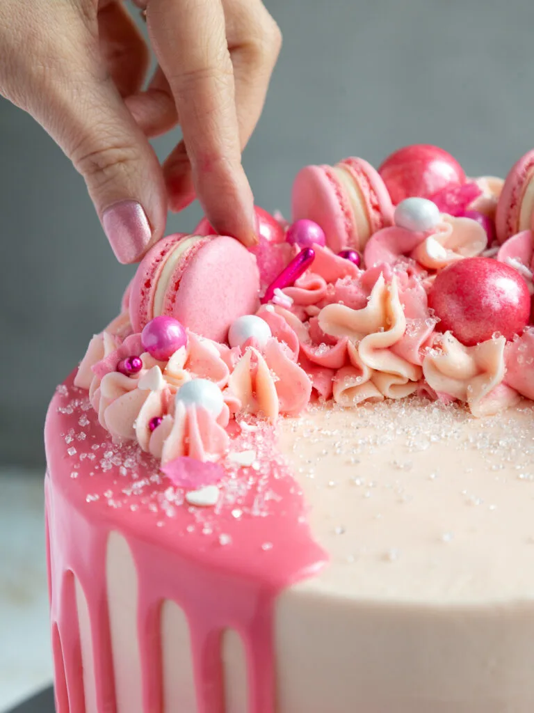 image of mini pink macarons being added to the top of a pretty pink birthday cake