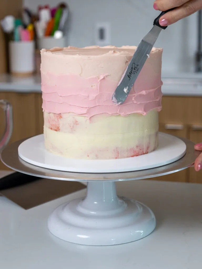 image of pink buttercream being spread around a pink cake with a small offset spatula
