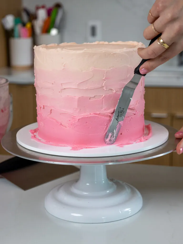 image of pink ombre buttercream frosting being spread on an ombre cake with a small offset spatula