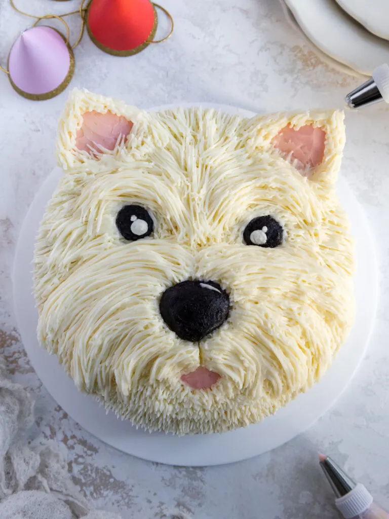 image is white buttercream fur being piped onto the ear of a westie dog cake