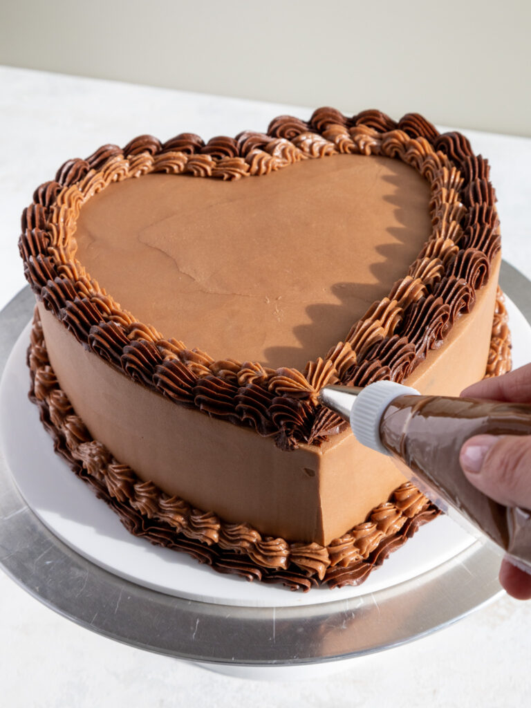 image of a shell border of chocolate buttercream being piped onto a heart shaped chocolate cake