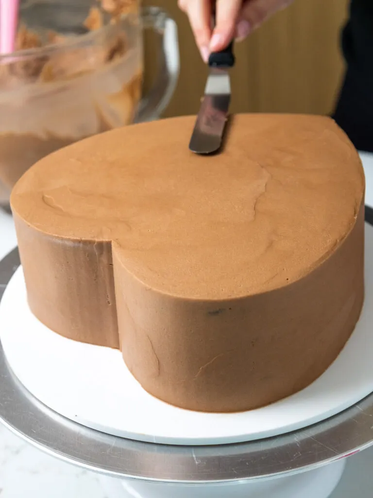 image of a heart shaped chocolate cake being frosted with a second coat of chocolate buttercream