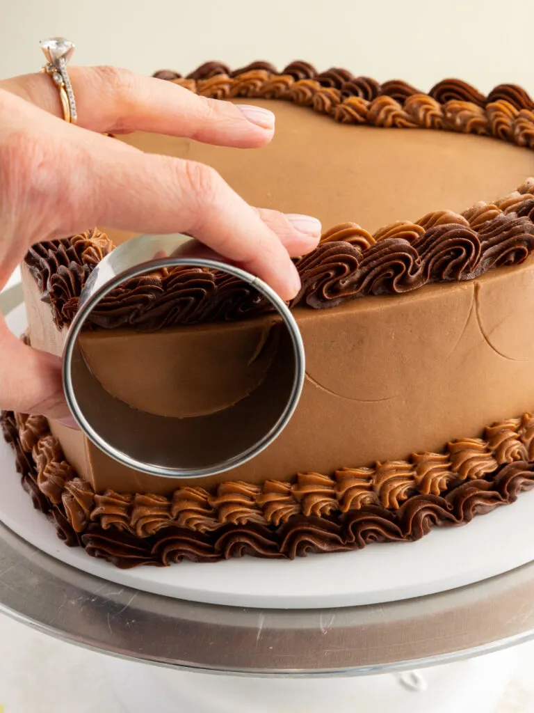 image of semi circles being traced around a heart shaped chocolate cake with a circle cookie cutter before being piped on with buttercream frosting