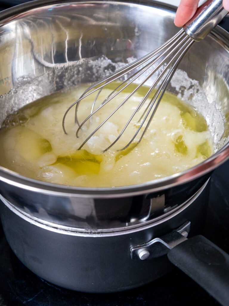 image of egg whites and granulated sugar being whisked together over a double boiler