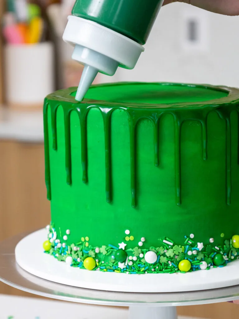 image of green ganache drips being added around a green cake