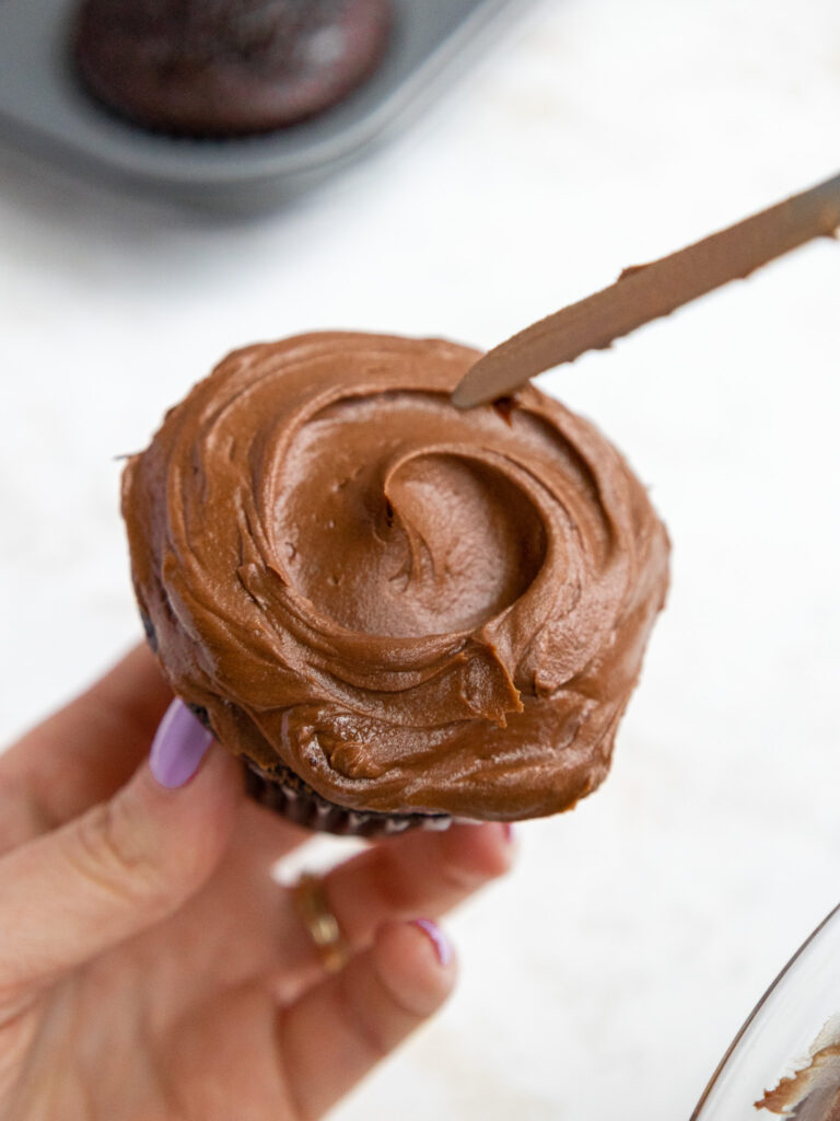 image of a swirl being added on top of a death by chocolate cupcake with a small offset spatula