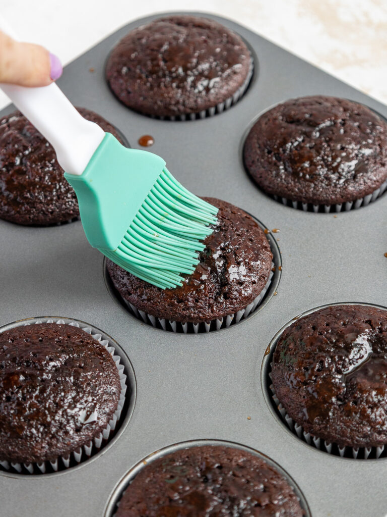 image of a dark chocolate cupcake being brushed with chocolate simple syrup
