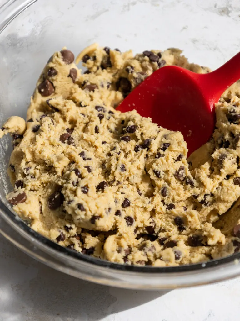 image of chocolate chips being mixed into cookie dough with a red rubber spatula