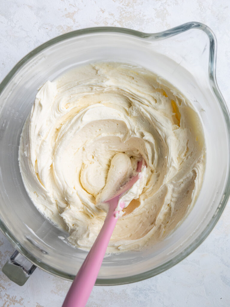 image of cream cheese frosting on a large glass bowl with a pink spatula