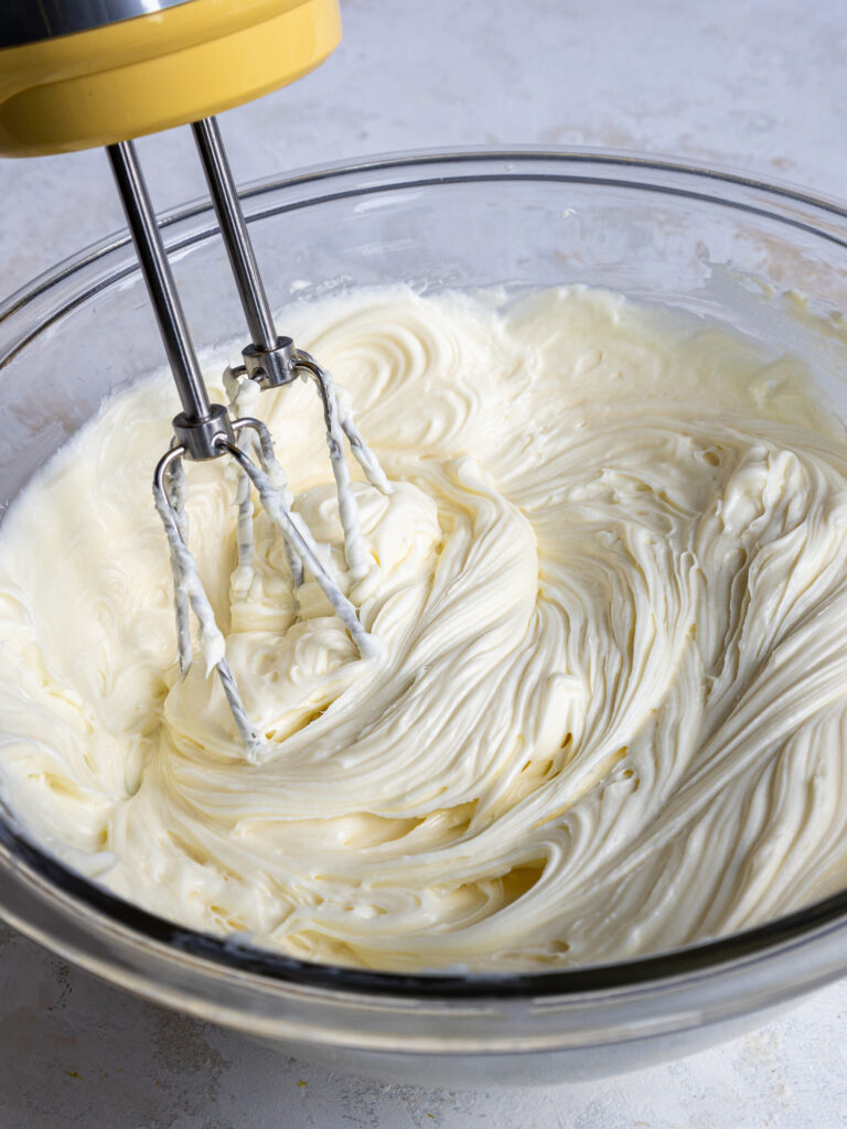 image of cream cheese and sugar being creamed together with a hand mixer