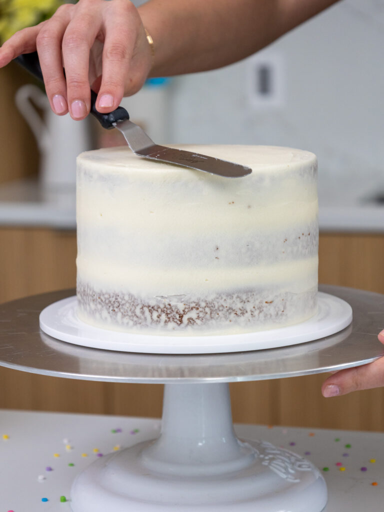 image of a small batch carrot cake being crumb coated with cream cheese frosting and a small offset spatula