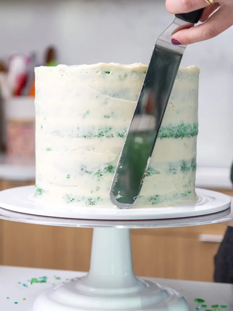 image of a green velvet cake that's being crumb coated with buttercream frosting