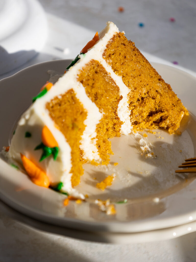 image of a slice of a 6-inch carrot cake on a plate that's been cut into with a fork